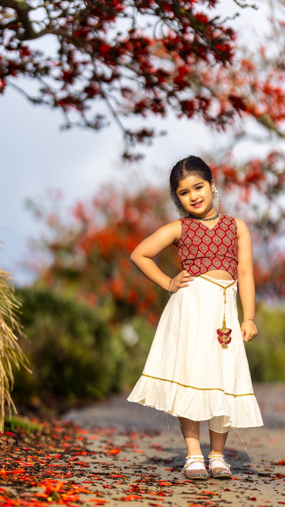 Child in traditional Onam attire photographed beneath red blossoms in Perth